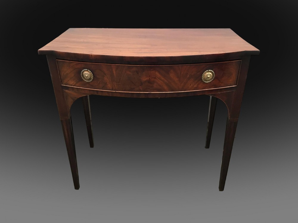 A late 18th-century George III mahogany bow front side table featuring a central drawer with circular brass handles and slender tapered legs.