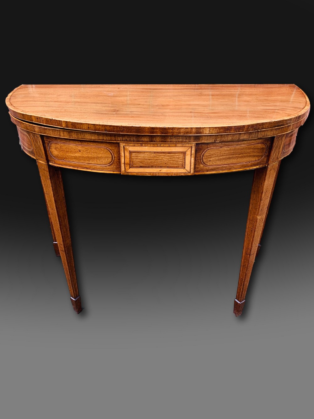A George III semi-circular mahogany card table featuring crossbanded inlay panels and square tapered legs.
