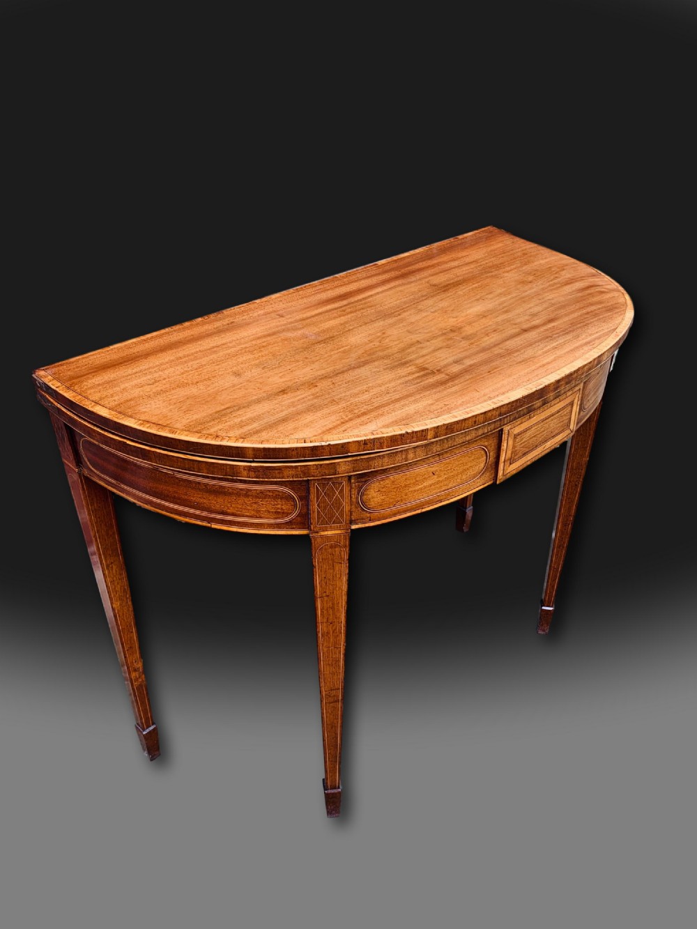 A George III semi-circular mahogany card table featuring crossbanded inlay panels and square tapered legs. View II