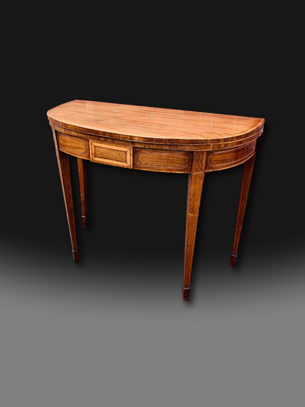 A George III semi-circular mahogany card table featuring crossbanded inlay panels and square tapered legs. View IV