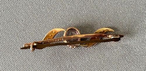 fig 1. An Edwardian 9ct gold bar brooch featuring a central oval faceted light purple amethyst set between flowing swirled accents inlaid with seed pearls.