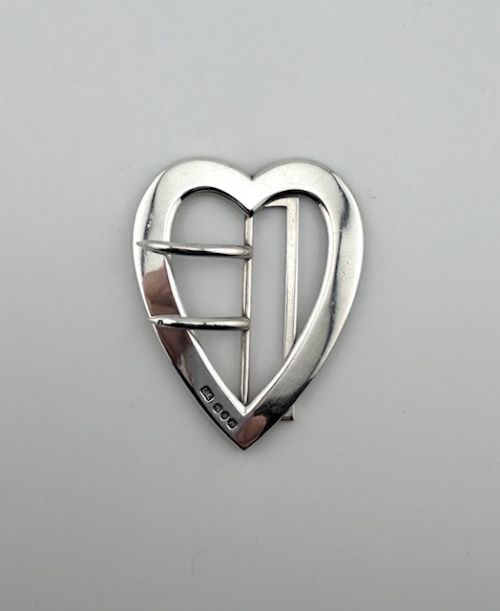 fig 1. A solid silver heart-shaped belt buckle featuring double prongs, a central crossbar, and visible British hallmarks stamped along the lower inner curve.