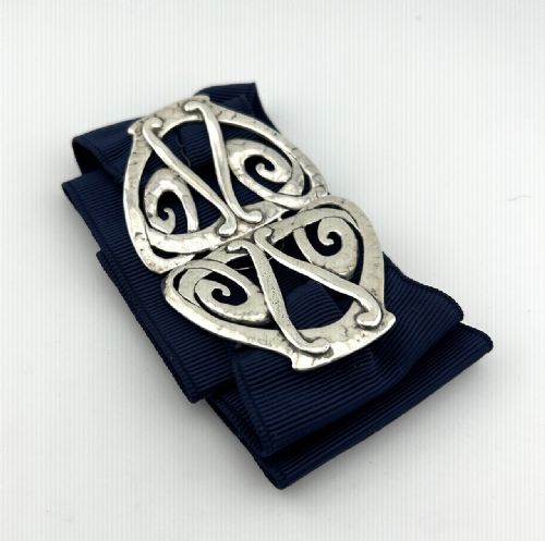 fig 1. An Edwardian Arts and Crafts style two-part silver belt buckle featuring openwork scroll motifs and a hand-hammered finish set on a navy ribbon.