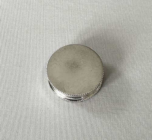 fig 1. A small circular George V sterling silver pill box featuring a milled rim and clear hallmark stamps.