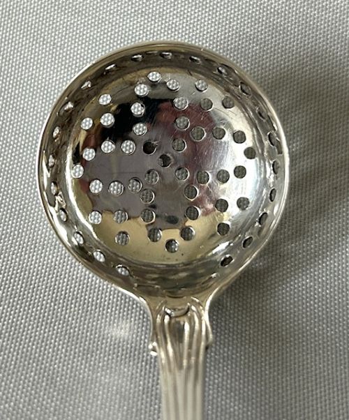 fig 1. A Georgian sterling silver sifting ladle featuring a round perforated bowl and a detailed shaped stem.