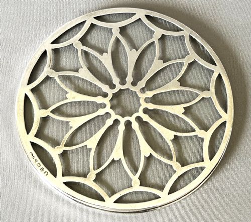 fig 1. A circular Art Deco teapot stand featuring pierced silver lattice design mounted over a clear glass base.