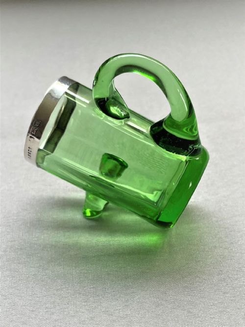 fig 1. A horizontal green glass vessel in a miniature tankard shape featuring a sterling silver rim and a glass handle.