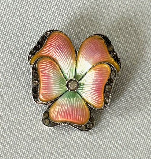 fig 1. An Edwardian flower-shaped silver brooch crafted with polychrome guilloche enamel in pink, orange, and green, surrounded by a marcasite border.