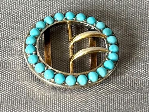 fig 1. An oval silver gilt buckle framed with round turquoise cabochons and fitted with a central double prong mechanism.