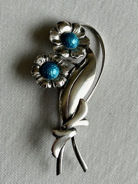 fig 1. A Danish sterling silver brooch featuring two stylized floral heads with blue enamel centres and a ribbon motif stem.