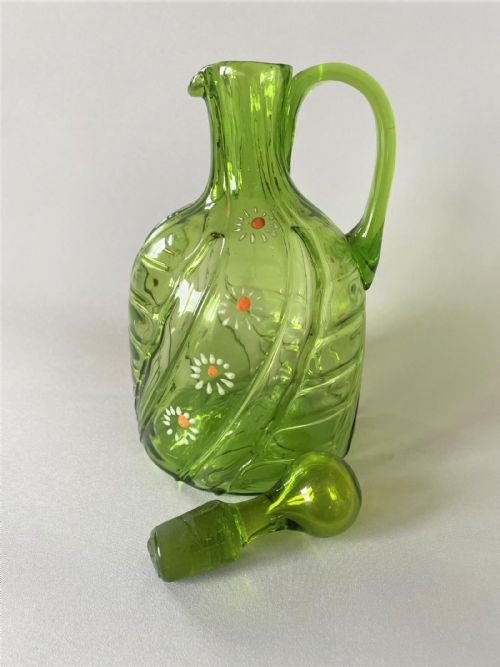 fig 1. A Victorian green glass wine jug featuring hand-painted white enamel daisy motifs, a swirled optic body, a loop handle, and a matching solid glass stopper.