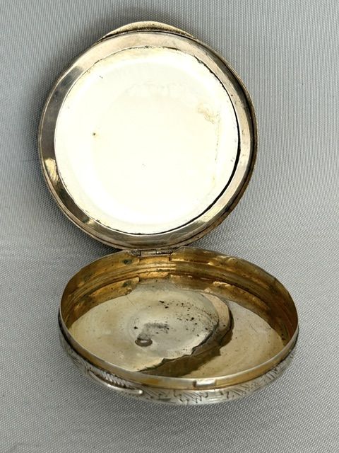 fig 2. A circular silver vanity compact featuring a hand-painted enamel pastoral scene framed by a turquoise border.