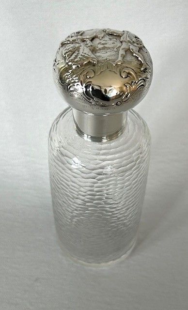 fig 1. A cylindrical textured clear glass cologne bottle featuring an embossed sterling silver stopper and collar.