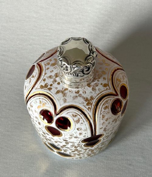 fig 1. An Edwardian Bohemian glass scent bottle featuring ruby red cut-outs over a white gilded pattern, topped with a hallmarked silver cap.