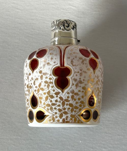 An Edwardian Bohemian glass scent bottle featuring ruby red cut-outs over a white gilded pattern, topped with a hallmarked silver cap. View IV