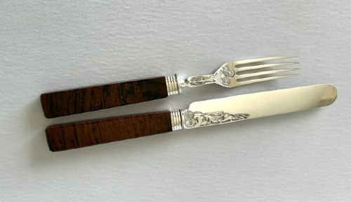 fig 1. A Victorian silver dessert knife and fork featuring engraved scrollwork on the blade and tines with polished rectangular dark brown agate handles.