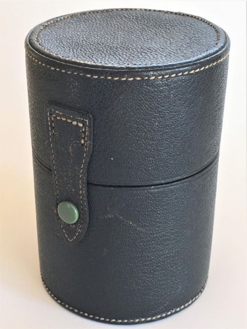 fig 1. Three wedge-shaped clear glass cologne bottles with silver caps resting beside an open cylindrical black leather travel case.