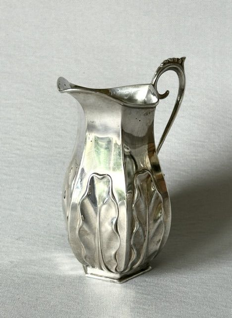 fig 1. A late Victorian silver cream jug featuring embossed relief leaf motifs around its lower body and a beaded scroll handle.