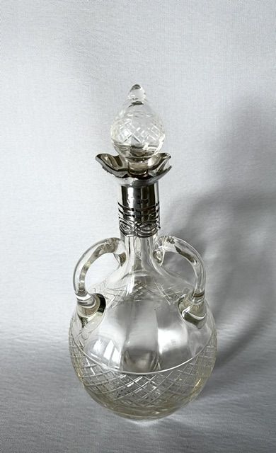 fig 1. An Edwardian clear cut glass decanter featuring double scroll handles, a diamond-cut lower body, and a hallmarked silver collar topped with a faceted glass stopper.