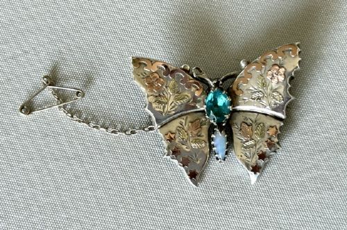A Victorian sterling silver butterfly brooch detailed with applied rose gold stars and floral motifs, set with a central oval green stone. View II