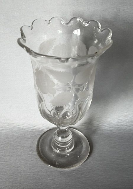 fig 1. A clear glass Victorian celery vase featuring an etched floral pattern, a scalloped frilled rim, and a stemmed circular foot.