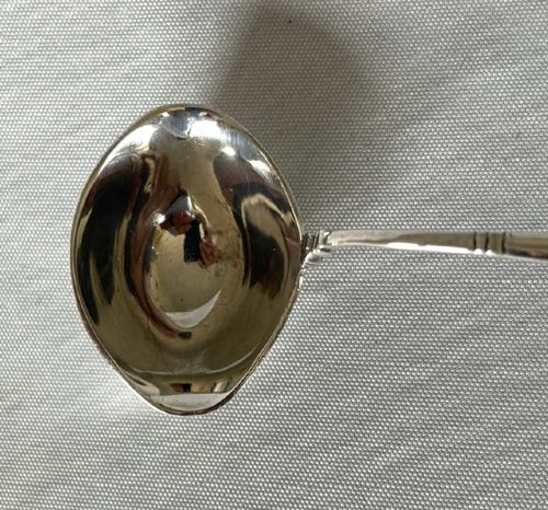fig 1. A sterling silver small sauce ladle featuring a rounded bowl attached to a tapered stem with a stylized acorn cap finial.