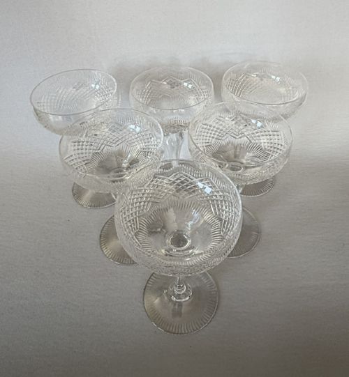 fig 1. A set of six clear cut glass champagne coupes featuring faceted stems and diamond-cut bowls arranged on a neutral background.