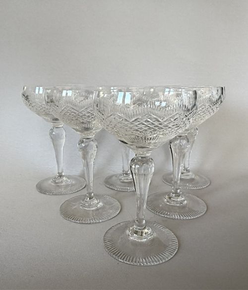 A set of six clear cut glass champagne coupes featuring faceted stems and diamond-cut bowls arranged on a neutral background. View III