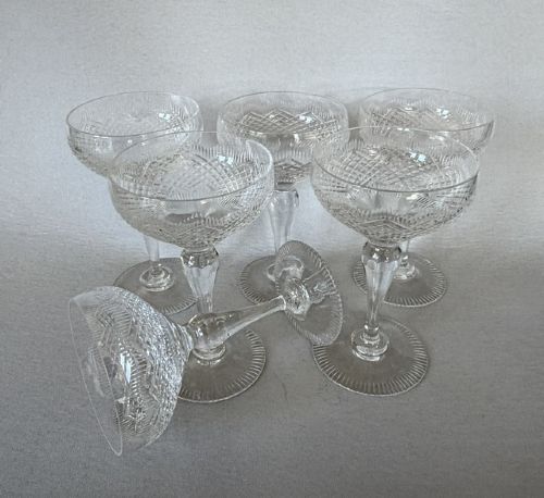 A set of six clear cut glass champagne coupes featuring faceted stems and diamond-cut bowls arranged on a neutral background. View IV