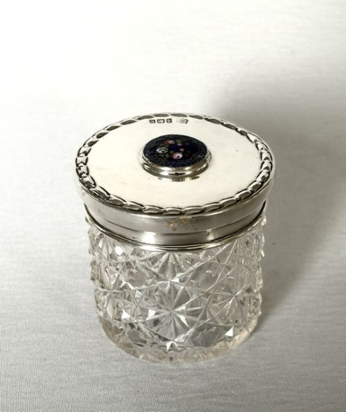 fig 1. A round cut glass vanity jar topped with a hallmarked sterling silver lid featuring a central blue floral enamel motif.
