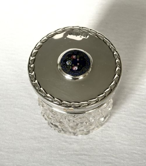 A round cut glass vanity jar topped with a hallmarked sterling silver lid featuring a central blue floral enamel motif. View IV