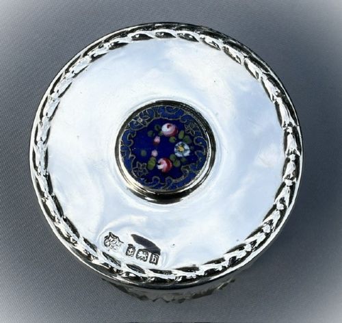 A round cut glass vanity jar topped with a hallmarked sterling silver lid featuring a central blue floral enamel motif. View VII