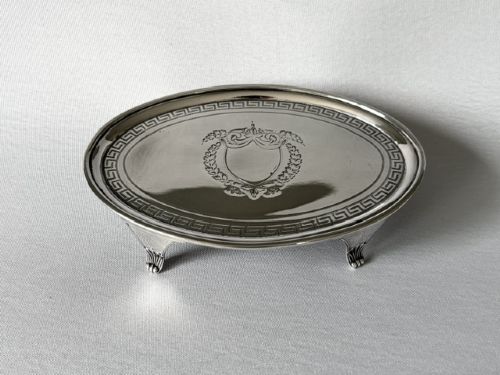 An oval Georgian silver teapot stand featuring an engraved Greek key border, a central cartouche, and four small supportive feet. View III