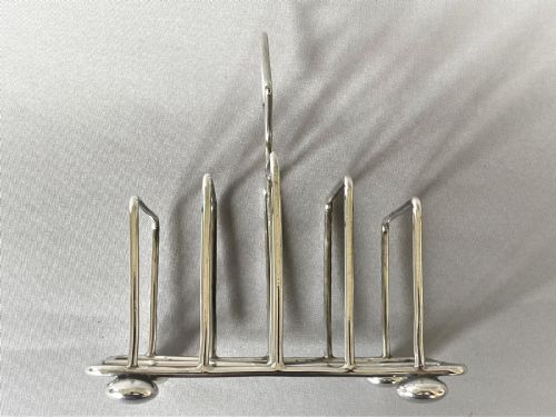fig 1. An Edwardian silver toast rack featuring four divisions, four ball feet, and a central diamond-shaped loop handle.