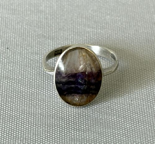 fig 1. A mid-century sterling silver ring featuring a large oval Blue John cabochon stone with distinct purple and cream banding, set in a plain bezel mount.