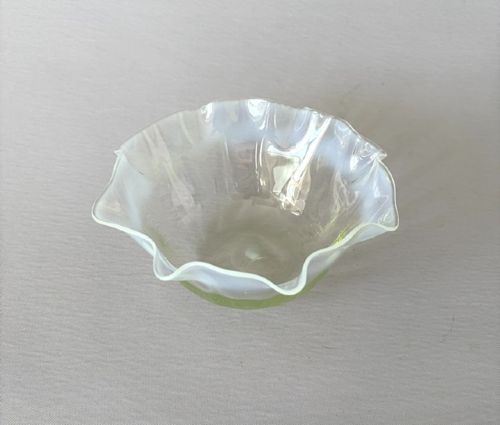 A small yellowish-green vaseline glass finger bowl featuring a flared ruffled rim with white opalescent shading. View III