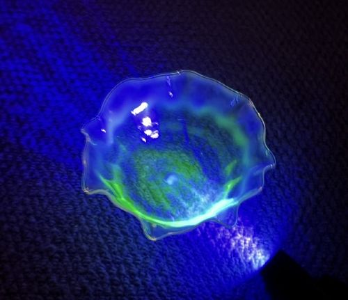 A small yellowish-green vaseline glass finger bowl featuring a flared ruffled rim with white opalescent shading. View VI