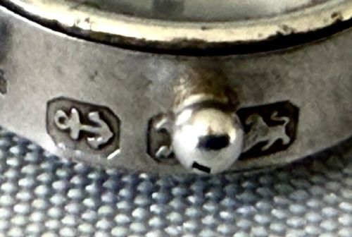 A miniature silver fob compass designed in the shape of a ships wheel with a central directional needle and suspension ring. View IV