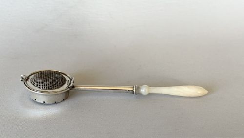 A late Victorian silver tea infuser featuring a circular mesh cage connected to a stem with a light-coloured carved handle. View III