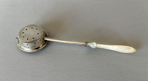 A late Victorian silver tea infuser featuring a circular mesh cage connected to a stem with a light-coloured carved handle. View IV