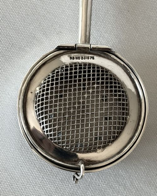 A late Victorian silver tea infuser featuring a circular mesh cage connected to a stem with a light-coloured carved handle. View VI