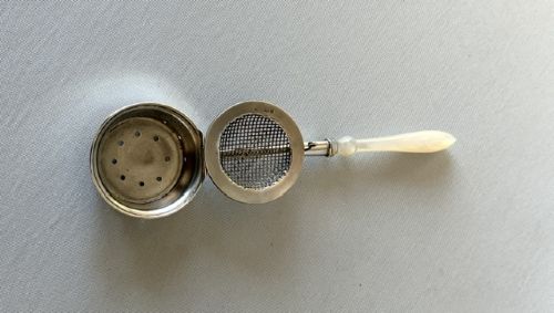 A late Victorian silver tea infuser featuring a circular mesh cage connected to a stem with a light-coloured carved handle. View VII