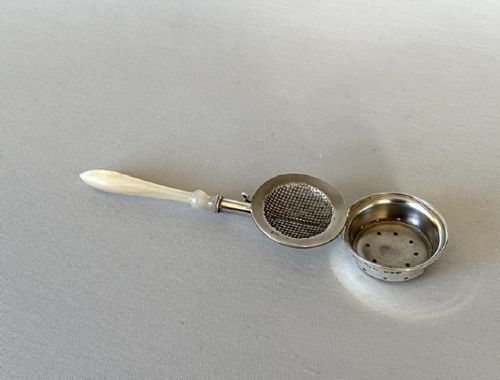 A late Victorian silver tea infuser featuring a circular mesh cage connected to a stem with a light-coloured carved handle. View VIII