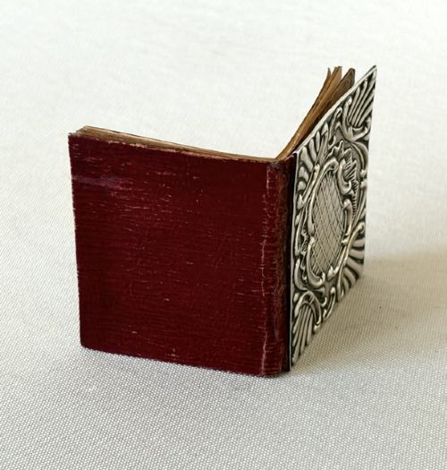 A miniature Edwardian book-shaped pocket calendar featuring an embossed silver front cover with detailed scrollwork and a central latticework pattern. View V