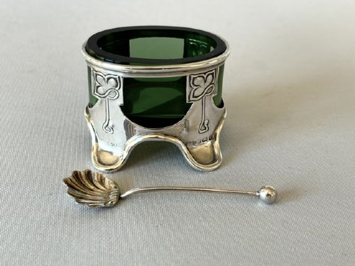 An Art Nouveau silver salt cellar frame featuring stylized organic motifs and resting on curved feet, housing a fitted green glass liner with an accompanying silver spoon. View III