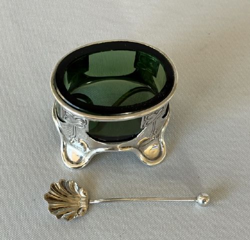 An Art Nouveau silver salt cellar frame featuring stylized organic motifs and resting on curved feet, housing a fitted green glass liner with an accompanying silver spoon. View IV
