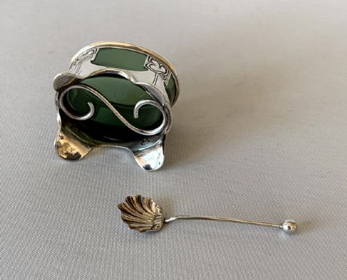 An Art Nouveau silver salt cellar frame featuring stylized organic motifs and resting on curved feet, housing a fitted green glass liner with an accompanying silver spoon. View VIII