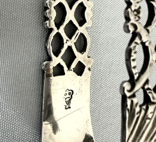 A pair of 18th-century cast silver sugar tongs featuring openwork lattice arms and shell-shaped grips. View VI