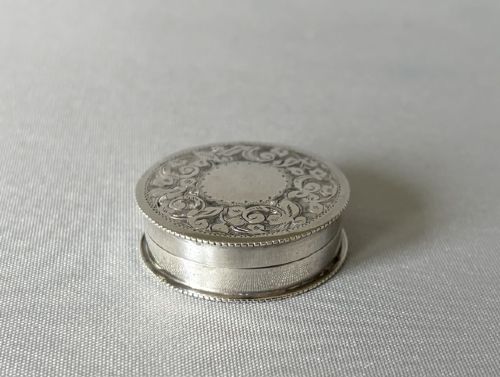 A small circular silver box featuring hand-engraved foliage and scroll patterns surrounding an unengraved circular centre. View III