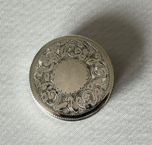 A small circular silver box featuring hand-engraved foliage and scroll patterns surrounding an unengraved circular centre. View VII